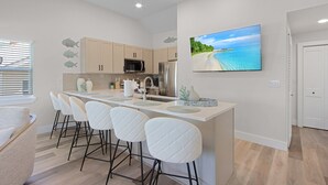 A modern kitchen with a central island, bar stools, and a large window. - Welcome To Coconut Dreams Fantastic Vacation Rental - 2633 Estero Blvd Unit A 3 Bedroom Home by RedAwning (Fort Myers Beach)
