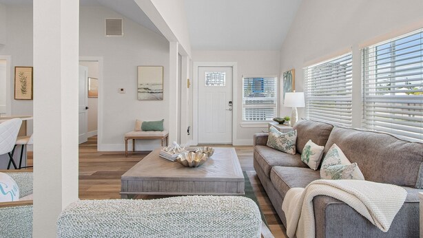 A spacious living room with a large window, a ceiling fan, and a wooden coffee table. - Welcome To Coconut Dreams Fantastic Vacation Rental - 2633 Estero Blvd Unit A 3 Bedroom Home by RedAwning (Fort Myers Beach)