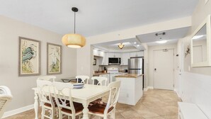 A modern kitchen with white cabinets, a central island, and a dining area with a white table and chairs. - ~fantastic Gulf Front Condo North Of The Pier~ 2 Bedroom Condo by RedAwning (Fort Myers Beach)