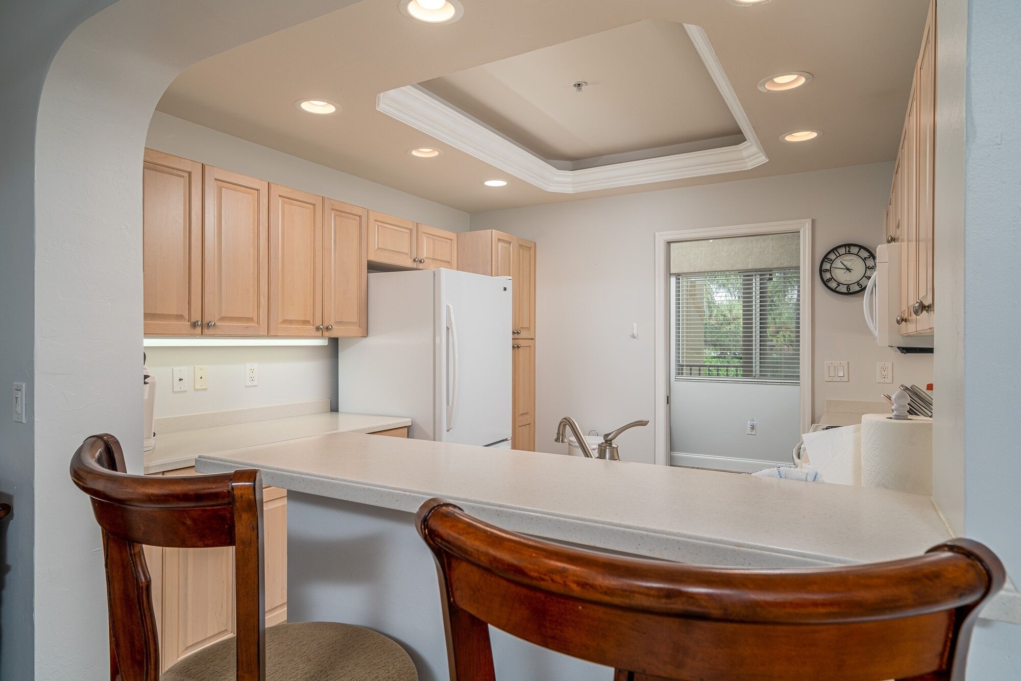 A kitchen with wooden cabinets, a white refrigerator, a sink, and a clock on the wall.
