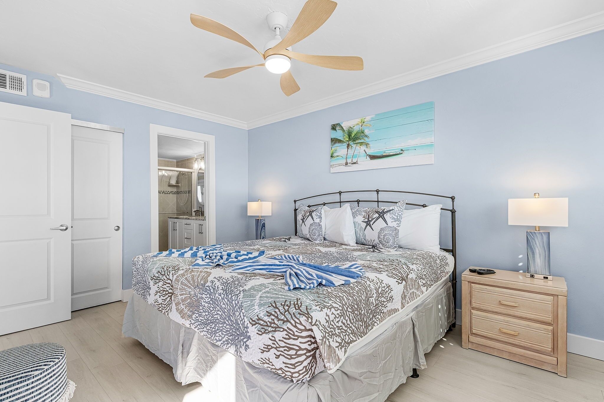 A bedroom with a bed, a ceiling fan, a nightstand, and a painting.