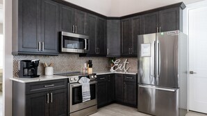 A modern kitchen with dark cabinets, stainless steel appliances, and a patterned backsplash. - Welcome To 5545 Palmetto Street All New! Just Built! Book It Now! 4 Bedroom Home by RedAwning (Fort Myers Beach)