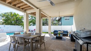 An outdoor patio with a dining table, chairs, a grill, and a pool in the background. - Welcome To 5545 Palmetto Street All New! Just Built! Book It Now! 4 Bedroom Home by RedAwning (Fort Myers Beach)