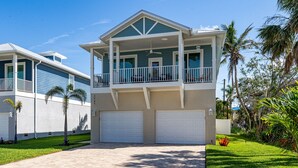 A two-story house with a balcony, two garages, and a well-maintained lawn. - Welcome To 5545 Palmetto Street All New! Just Built! Book It Now! 4 Bedroom Home by RedAwning (Fort Myers Beach)