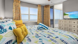A bedroom with a bed, curtains, a television, and a view of the sea.