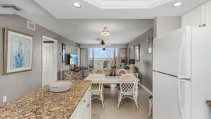 A kitchen with granite countertops, white cabinetry, a dining area with white chairs, and a large window offering a view.