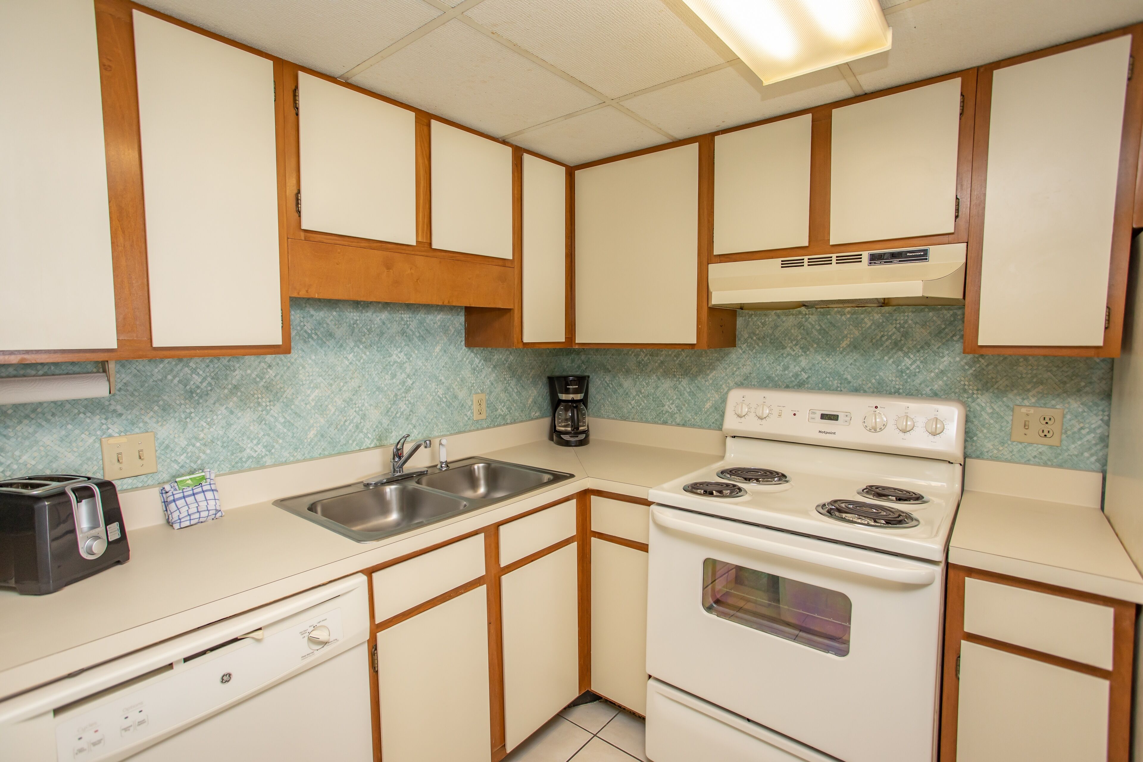 A compact kitchen with white cabinets, a stove, a sink, and a toaster.