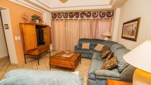 A living room with a sofa, a coffee table, a TV stand, and a lamp. - Luxurious 1 Bedroom Condo on Sandy Beach at Las Palmas Resort B-402 1 Condo by RedAwning (Puerto Peñasco)