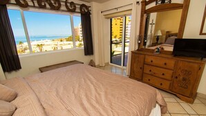 A bedroom with a large bed, a wooden dresser, a television, and a view of the beach through a sliding glass door. - Luxurious 1 Bedroom Condo on Sandy Beach at Las Palmas Resort B-402 1 Condo by RedAwning (Puerto Peñasco)