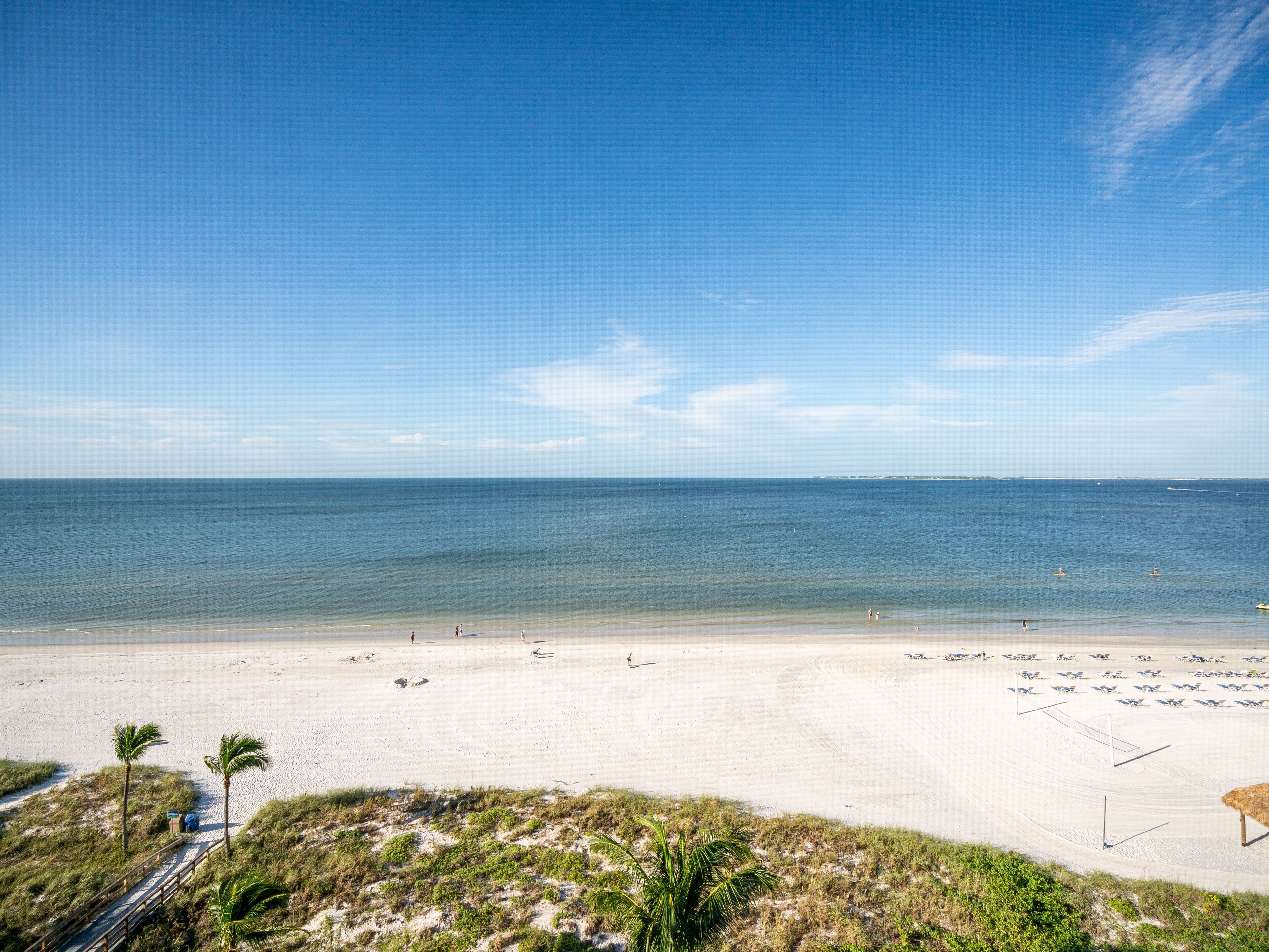 A beach with a clear sky, calm sea, and a sandy shore with some vegetation.