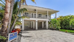 A two-story coastal vacation property with a covered patio, palm trees, and a paved driveway. - Welcome To 246 Delmar Ave - Vacation Rental 3 Bedroom Home by RedAwning (Fort Myers Beach)