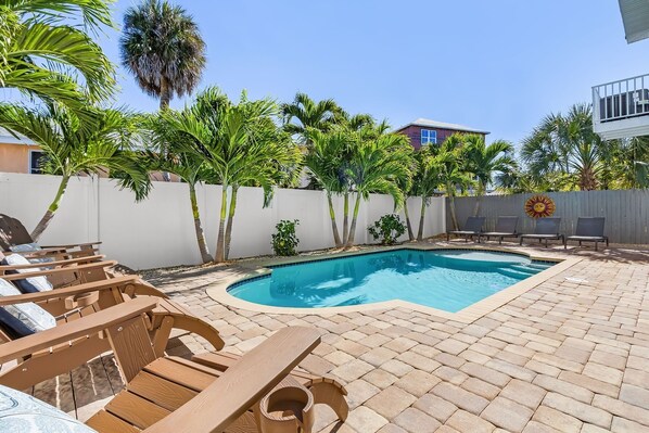 Un patio trasero con piscina, sillones de madera y palmeras.