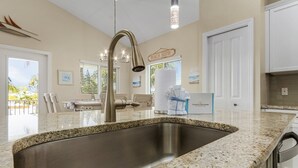 A kitchen with a granite countertop, stainless steel sink, and a 'Beach House' sign. - Welcome To 246 Delmar Ave - Vacation Rental 3 Bedroom Home by RedAwning (Fort Myers Beach)