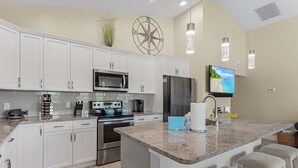 A modern kitchen with white cabinets, stainless steel appliances, a granite countertop, and a large island with bar stools. - Welcome To 246 Delmar Ave - Vacation Rental 3 Bedroom Home by RedAwning (Fort Myers Beach)