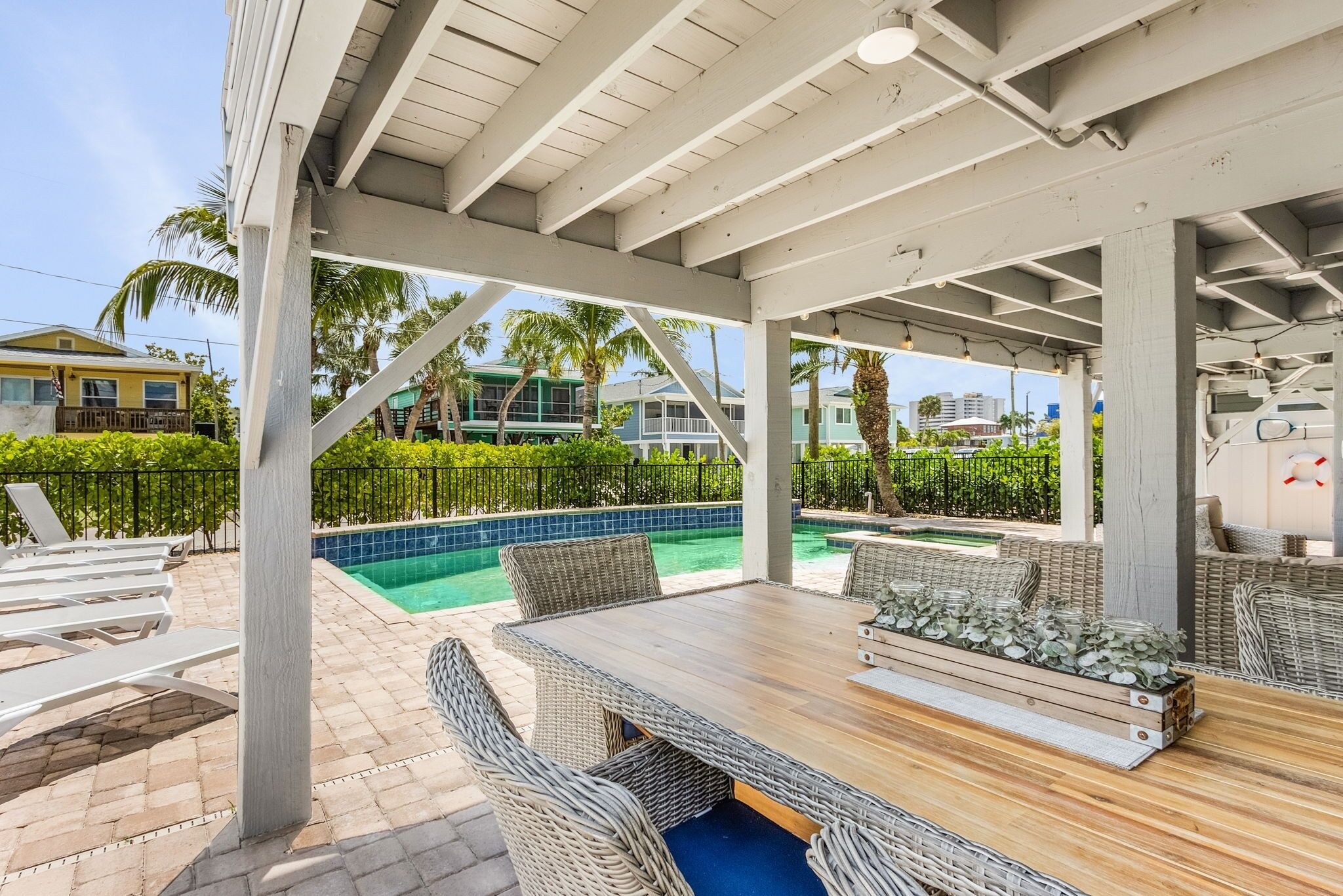 An outdoor patio with a pool, wicker furniture, and a wooden table.