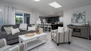 A modern living room with a grey sofa, striped armchair, and a white coffee table. There is a kitchen area with dark cabinets and a dining set. - Shells N Sunshine! Getaway Destination Just Minutes From The White Sandy Beaches Of Fort Myers! 4 Bedroom Home by RedAwning (Fort Myers Beach)