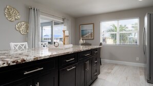 A modern kitchen with a marble countertop, black cabinets, and a large window with blinds. - Shells N Sunshine! Getaway Destination Just Minutes From The White Sandy Beaches Of Fort Myers! 4 Bedroom Home by RedAwning (Fort Myers Beach)