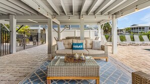 A covered outdoor seating area with a sofa, a coffee table, and a poolside view. - Shells N Sunshine! Getaway Destination Just Minutes From The White Sandy Beaches Of Fort Myers! 4 Bedroom Home by RedAwning (Fort Myers Beach)