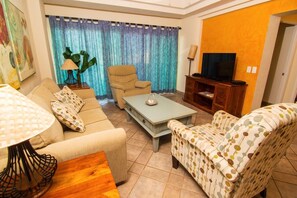 Una sala de estar con sofá, sillón, mesa de centro, mueble para televisión y cortinas.