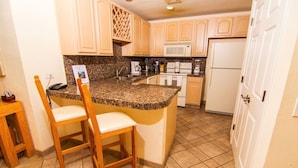 A kitchen with granite countertops, wooden chairs, a microwave, a refrigerator, and a sink. - Spectacular 2 Bedroom Condo on Sandy Beach at Las Palmas Resort B-203 2 Condo by RedAwning (Puerto Peñasco)