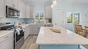 A modern kitchen with white cabinets, a large island, stainless steel appliances, and a blue-tiled backsplash. - Welcome To Mermaid Bay Vacation Rental - 261 Delmar 3 Bedroom Home by RedAwning (Fort Myers Beach)