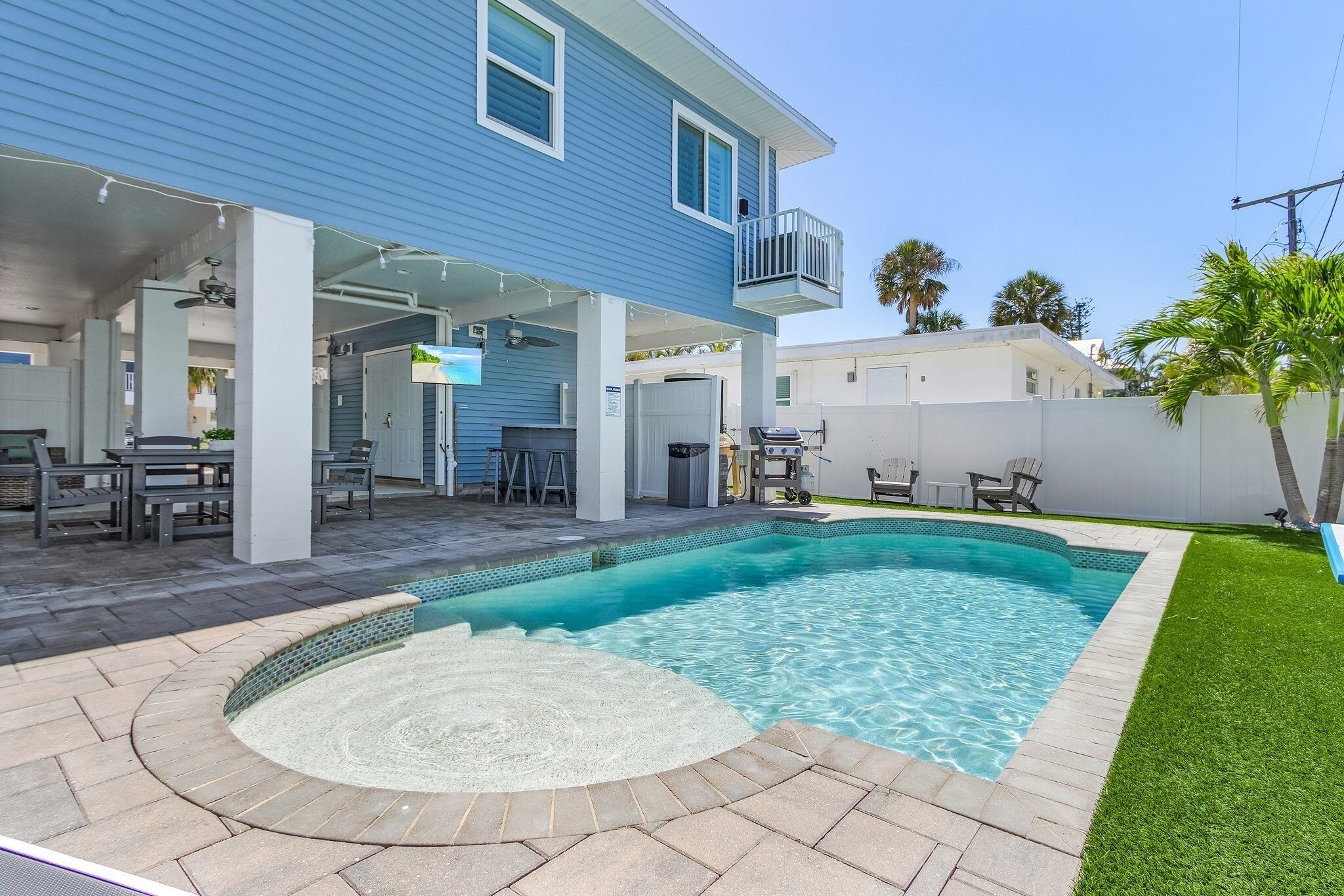A backyard with a swimming pool, patio furniture, and a covered seating area.