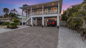 A two-story house with a covered driveway and a red vehicle parked inside. - Welcome To Mermaid Bay Vacation Rental - 261 Delmar 3 Bedroom Home by RedAwning (Fort Myers Beach)