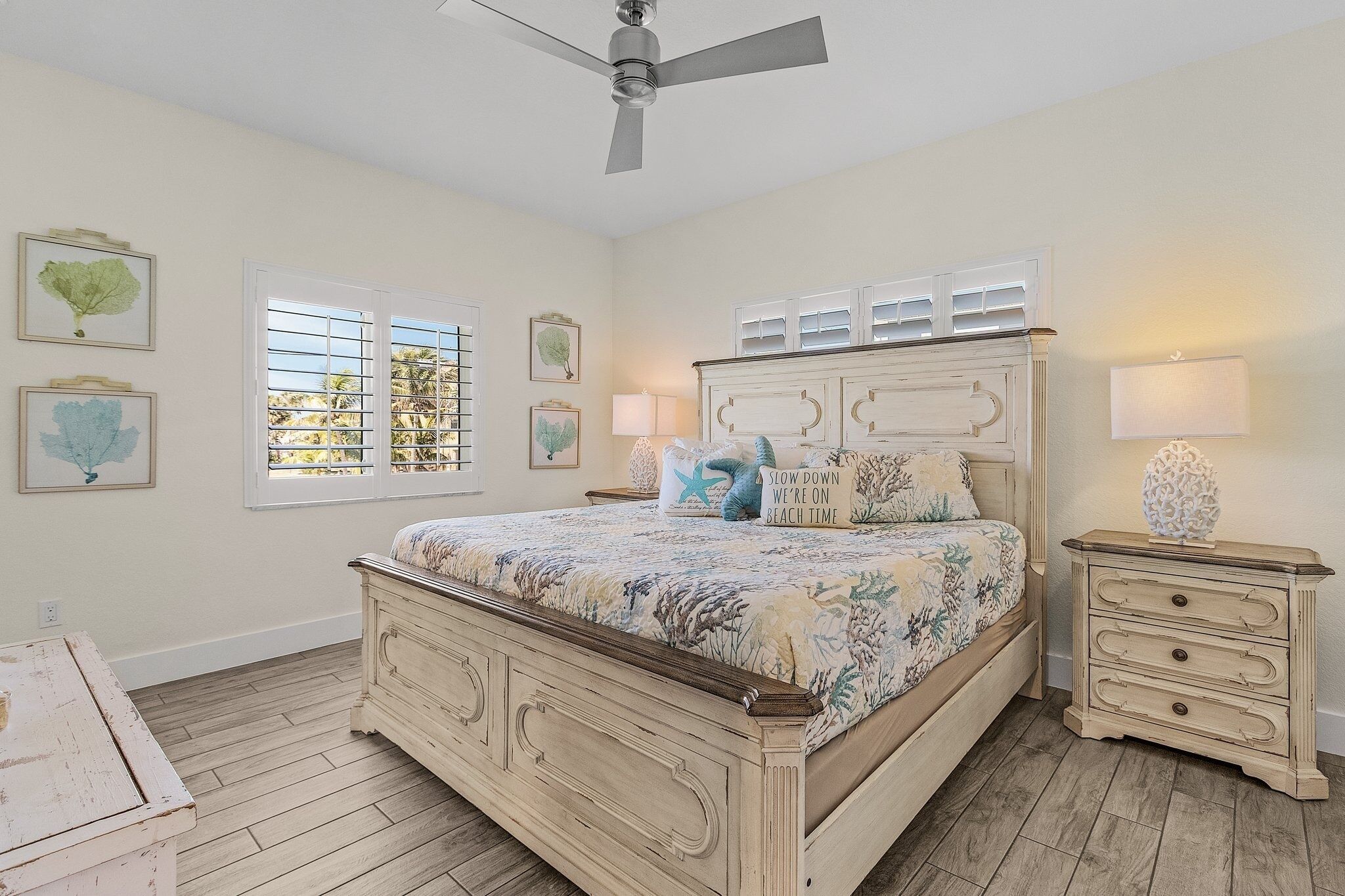 A bedroom with a bed, bedside tables, a ceiling fan, and windows with blinds.