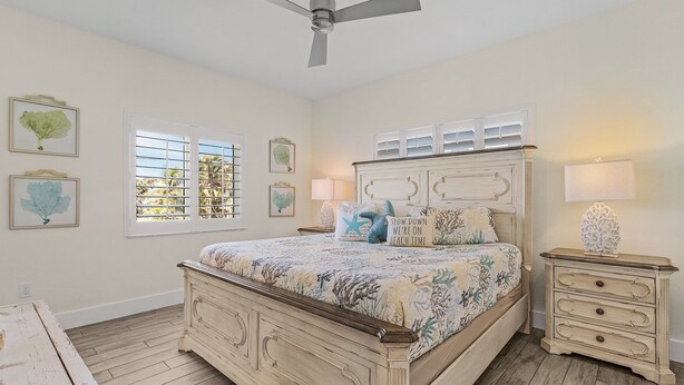 A bedroom with a bed, bedside tables, a ceiling fan, and windows with blinds. - Welcome To Mermaid Bay Vacation Rental - 261 Delmar 3 Bedroom Home by RedAwning (Fort Myers Beach)