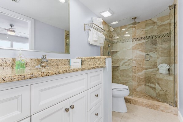 Un baño moderno con encimera de granito, ducha con mampara de vidrio y un inodoro blanco.