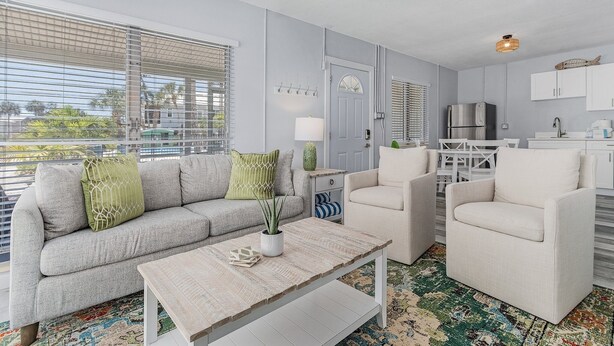 A modern living room with a grey sofa, two armchairs, a coffee table, and a kitchen area in the background. - 171 Washington ~ Dune Our Thing ~ Unit D ~ Fabulous Pool Home! 2 Bedroom Home by RedAwning (Fort Myers Beach)
