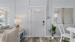 A modern living room with a white door, a lamp, a potted plant, and a white chair. - 171 Washington ~ Dune Our Thing ~ Unit D ~ Fabulous Pool Home! 2 Bedroom Home by RedAwning (Fort Myers Beach)