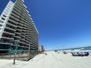 Et hotel ved stranden med flere balkoner og en sandstrand i baggrunden.