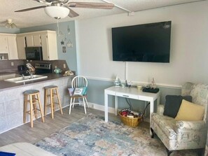 Um espaço compacto para viver, com cozinha compacta, área de refeições, TV na parede e tapete estampado.