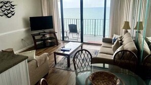 A living room with a television, a sofa, a coffee table, and a view of the sea through large windows.