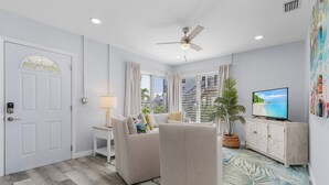 A modern living room with a sofa, TV, and a ceiling fan. - 171 Washington ~ Dune Our Thing ~ Unit A ~ Fabulous Pool Home! 2 Bedroom Home by RedAwning (Fort Myers Beach)