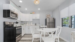 A modern kitchen with white cabinetry, a black stove, and a stainless steel refrigerator. - 171 Washington ~ Dune Our Thing ~ Unit A ~ Fabulous Pool Home! 2 Bedroom Home by RedAwning (Fort Myers Beach)