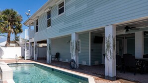 Una piscina con suelo de baldosas, un patio cubierto con sillas y una palmera.