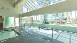 An indoor swimming pool with clear glass walls, a separate hot tub area, and a view of the cityscape through large windows. - Royal Garden Resort 803 1 Bedroom Condo by RedAwning (Murrells Inlet)