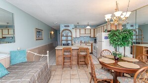 A compact kitchen with a central island, wooden chairs, and a dining table. - Royal Garden Resort 803 1 Bedroom Condo by RedAwning (Murrells Inlet)