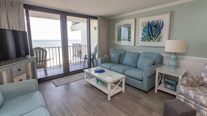 Un salon comprenant un canapé, une table basse, un téléviseur et un balcon avec vue sur l’océan.