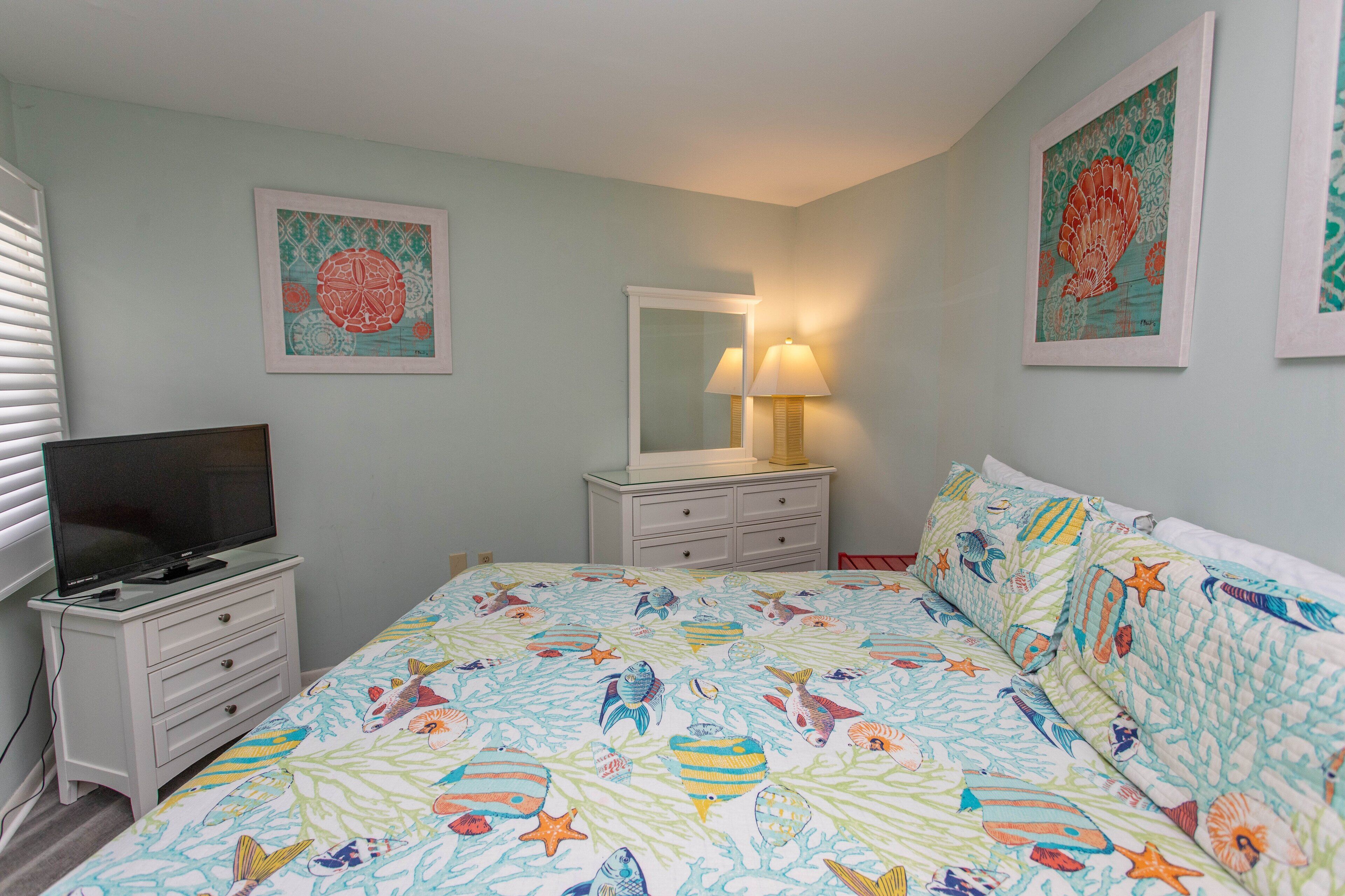 Een slaapkamer met een bed, een televisie op een dressoir, een spiegel en kunstwerken aan de muren.