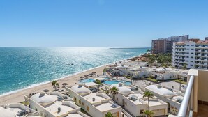 Un resort con varias edificaciones blancas, un área de piscina central y una playa con sombrillas.
