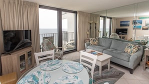 Una sala de estar con un televisor grande, una mesa de comedor con platos, un sofá y un balcón con vistas.