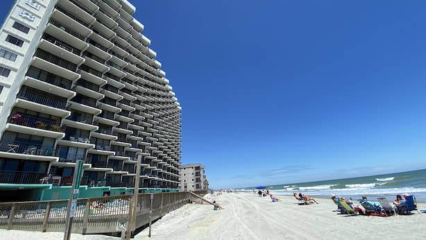 Un hotel frente a la playa con varios balcones y una playa de arena al fondo.