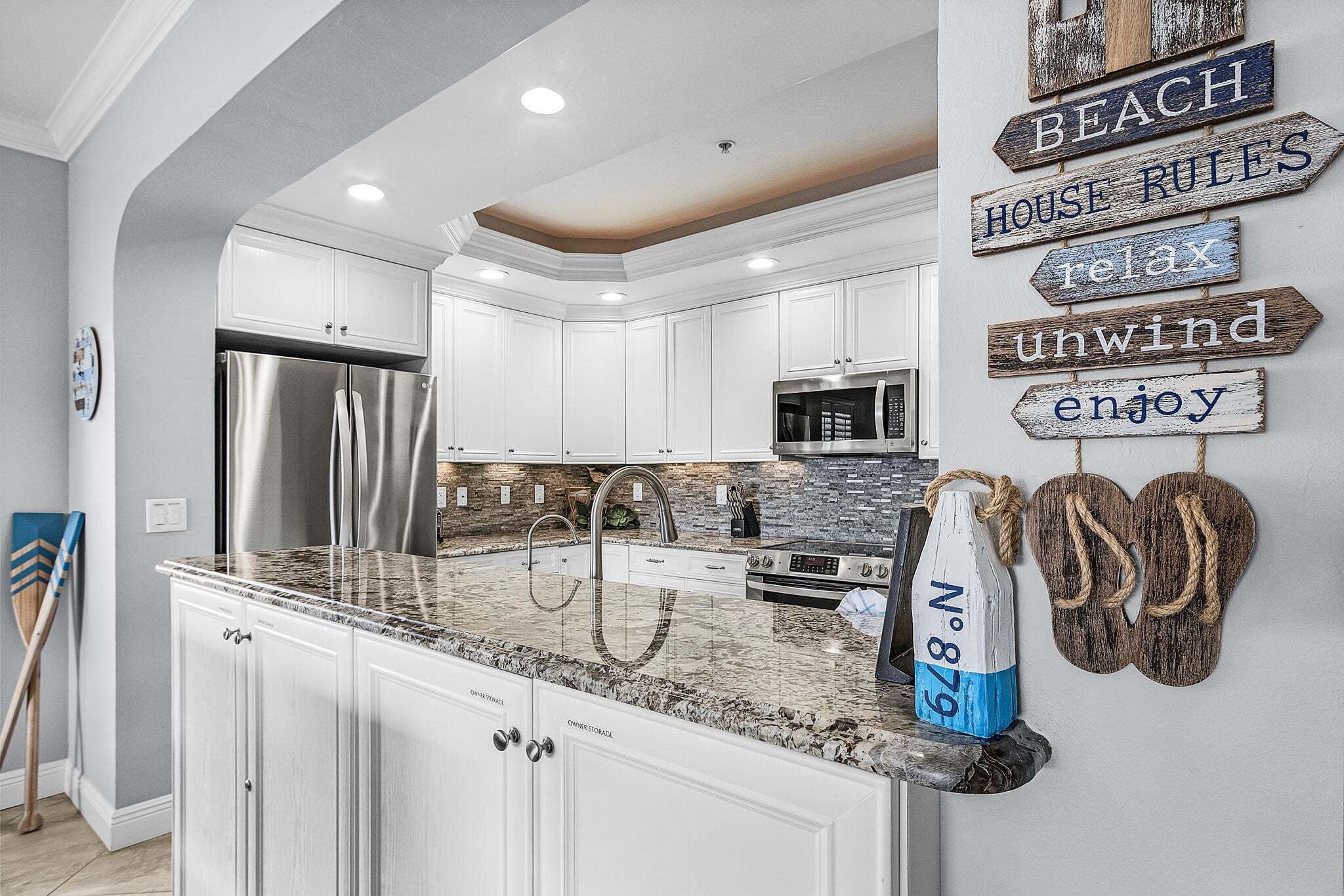 A modern kitchen with white cabinetry, granite countertops, stainless steel appliances, and decorative signs on the wall.
