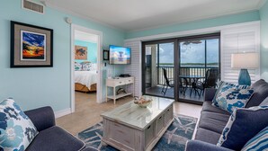 A living room with a large sliding glass door leading to a balcony, a television, and a dining area with outdoor seating. - Welcome To Carlos Point # 324 2 Bedroom Condo by RedAwning (Fort Myers Beach)