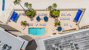 An aerial view of a hotel with a swimming pool, sun loungers, and palm trees. - Welcome To Carlos Point # 324 2 Bedroom Condo by RedAwning (Fort Myers Beach)