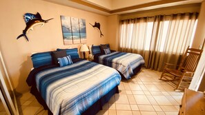 Una habitación de hotel con dos camas, un sillón mecedor y obras de arte en las paredes.