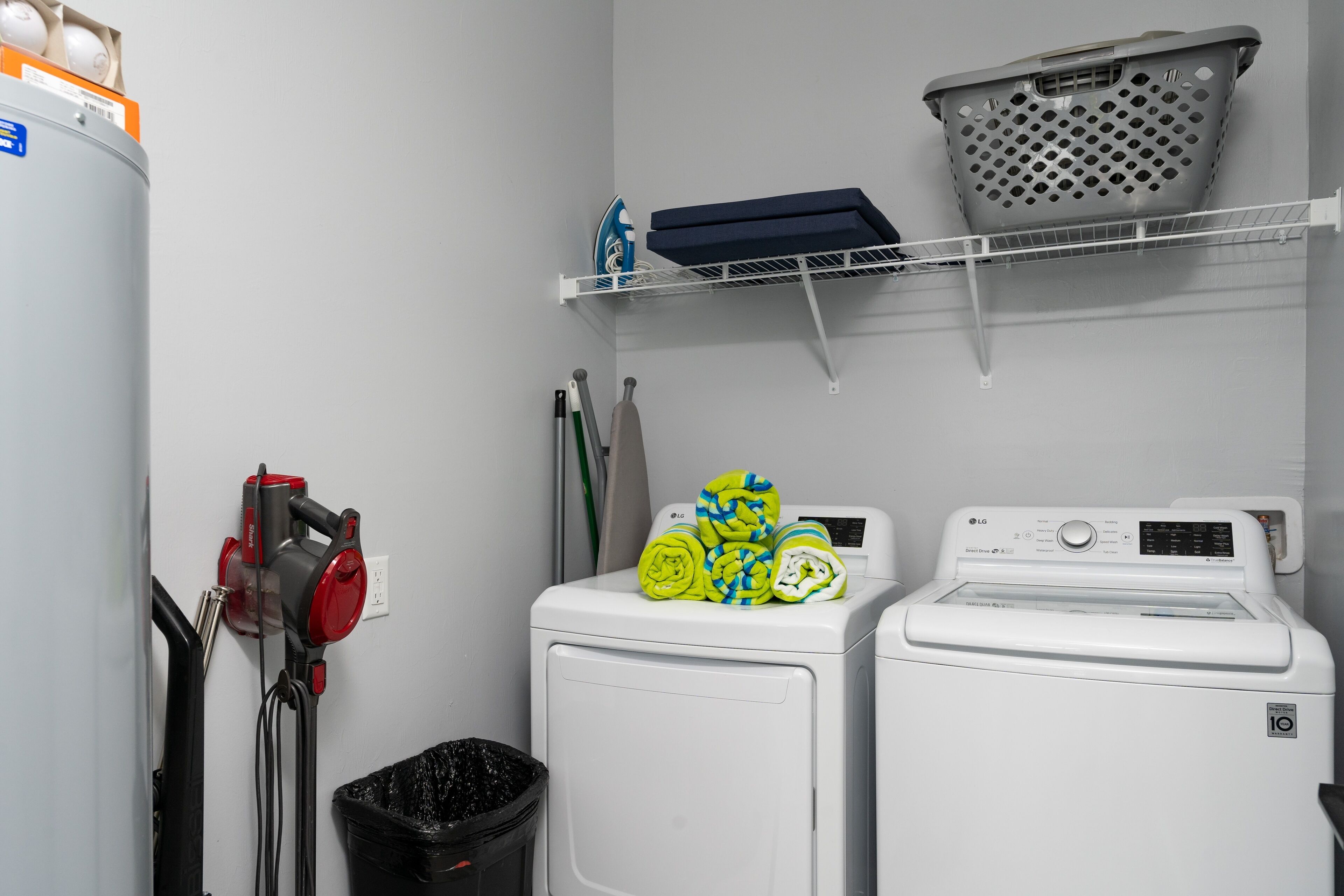 A laundry area with two washing machines, a drying rack, and a trash bin.